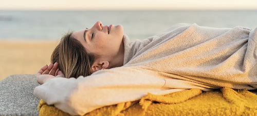 A woman lying on a beach with her eyes closed, looking completely relaxed.
